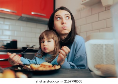 
Tired Mom Trying to Feed Her Toddler Daughter in the Kitchen. Stressed parent having a hard time at the dinner table
