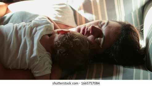 
Tired Mother Asleep On Sofa With Baby Infant. Real Life Authentic Mom Napping With Child