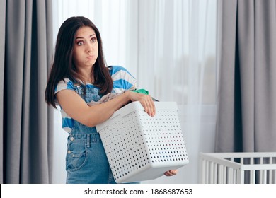 Tired Mother Holding A Basket Of Dirty Laundry In Nursery Room. New Mom Feeling Exhausted Dealing With Household Chores
