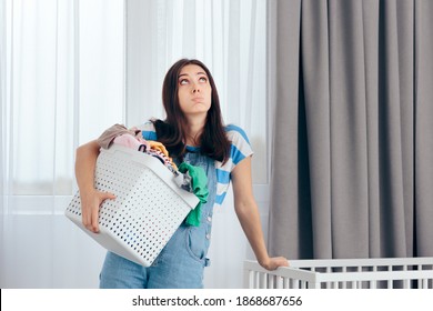 Tired Mother Holding A Basket Of Dirty Laundry In Nursery Room. New Mom Feeling Exhausted Dealing With Household Chores
