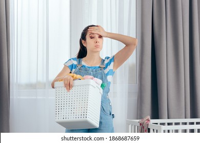 Tired Mother Holding A Basket Of Dirty Laundry In Nursery Room. New Mom Feeling Exhausted Dealing With Household Chores
