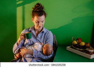 Tired Mother In Kitchen At The Table Puts Her Newborn To Sleep. Mom Rocks The Baby And Sings A Lullaby. Caring For Baby Hug Tenderness. Sleep Deprivation Insomnia Drink Coffee. Night Dawn Dim. 