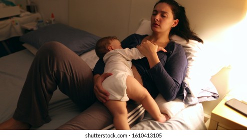 Tired Mother Laid In Bed With Baby Infant At Night. Authentic Real Life Exhausted Parent Taking Rest With Toddler Child