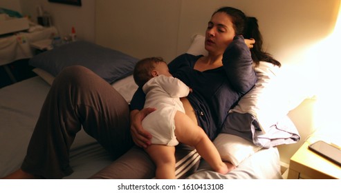 Tired Mother Laid In Bed With Baby Infant At Night. Authentic Real Life Exhausted Parent Taking Rest With Toddler Child