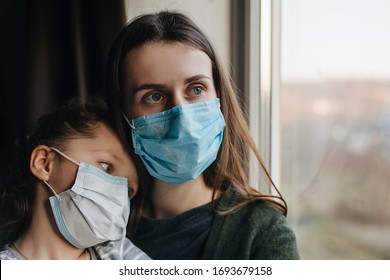 Tired mother and little daughter in medical sterile face mask sitting on sill looking at window, sad family spending time alone at home. Concept of coronavirus or COVID-19 pandemic disease symptoms - Powered by Shutterstock