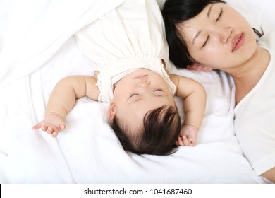 Tired mother sleeping with her baby daughter laying on the bed at home.
