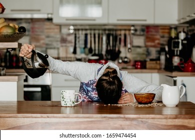 Tired Mother, Trying To Pour Coffee In The Morning. Woman Lying On Kitchen Table After Sleepless Night, Trying To Drink Coffee