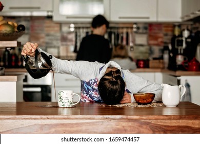 Müde Mutter, versucht, Kaffee am Morgen zu gießen. Frau liegt nach schlafloser Nacht auf dem Küchentisch und versucht Kaffee zu trinken