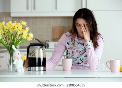 Tired Mother, Trying To Pour Coffee In The Morning. Woman Lying On Kitchen Table After Sleepless Night, Trying To Drink Coffee