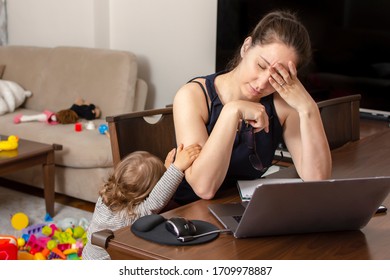 Tired mother trying to work on a laptop at home during her kid crying. Childcare and working mom concept. Women powerful. Toddler tantrum. Young lady working at home during quarantine.