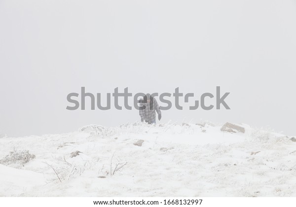 Tired mountain hiker with\
rubber boots and hood walking through the misty, snow covered\
highlands