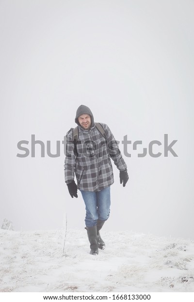 Tired mountain hiker with\
rubber boots and hood walking through the misty, snow covered\
highlands