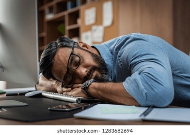 Tired multiethnic businessman sleeping in office. Middle eastern business man with eyeglasses worked late and fell asleep on the computer keyboard. Creative casual man sleeping at his working place