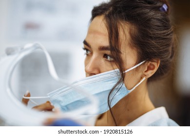 Tired Nurse Takes Off A Protective Face Shield And Medical Mask After A Tough Working Shift At The Hospital. Female Doctor Fights The Coronavirus Pandemic Working Hard Overtime And Being Exhausted