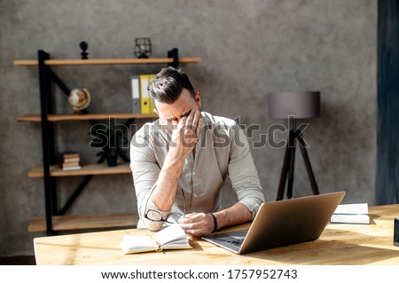 Tired office worker with a laptop. He took off the glasses and is rubbing his eyes tired from all the computer work. Laptop and notebook are n front of him on the table Foto stock © 