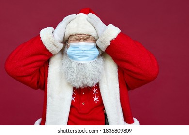 Tired Old Bearded Ill Santa Claus In Panic Wearing Costume, Face Mask Feeling Headache, Stress, Getting Sick On Christmas Holidays Standing On Red Background. Covid 19 Coronavirus Problem Concept.