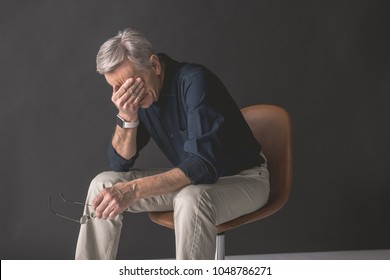 Tired old man closing face by hand while locating on seat. Fatigue during job concept