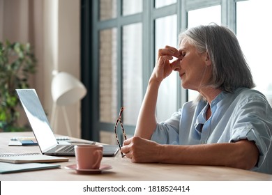 Tired Old Senior Business Woman Taking Off Glasses Suffers From Eyestrain, Stress, Headache, Fatigue After Computer Use Work In Office. Exhausted Sick Mature Lady Feels Eye Strain Problem At Workplace