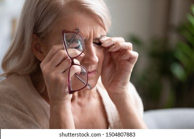 Tired older woman taking off glasses, feeling eye strain, touching eyelids close up, unhappy exhausted mature female suffering from dry eyes syndrome, vision health problem concept