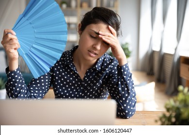 Tired Overheated Young Indian Woman Hold Wave Fan Suffer From Heat Sweating Indoor Work On Laptop At Home Office, Annoyed Girl Feel Uncomfortable Hot Summer Weather Problem No Air Conditioner Concept