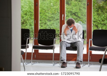 Tired and overworked doctor or medical specialist with surgical mask sitting in an empty waiting room