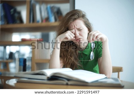 tired overworked, exhausted young woman in glasses college or university student is study hard in library, lesson, problem with eyes, myopic purblind. Vision eyes problems, myopia, blindness. 