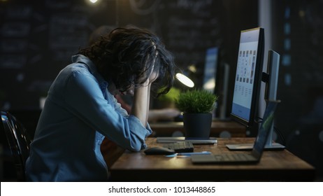 Tired, Overworked Female Mobile Phone App Designer Holds Her Head in Hands while Working on a Personal Computer. In the Background Creative Office. - Powered by Shutterstock