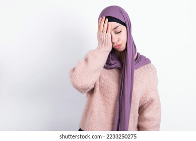 Tired overworked muslim woman wearing hijab and knitted sweater over white background has sleepy expression, gloomy look, covers face with hand, has eyes shut, gasps from tiredness, fatigue  - Shutterstock ID 2233250275