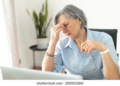 Tired and overworked stressed mature woman working on laptop at home indoor, female teacher feeling exhausted after lecturing students online, touching eyes. Smart working senior people and technology - Powered by Shutterstock