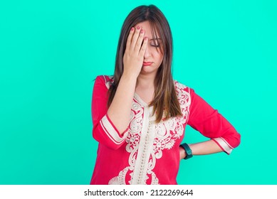 Tired Overworked Young Beautiful Moroccan Woman Wearing Traditional Caftan Dress Over Green Background Has Sleepy Expression, Gloomy Look, Covers Face With Hand, Has Eyes Shut, Gasps From Tiredness.