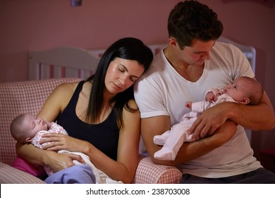 Tired Parents Cuddling Twin Baby Daughters In Nursery