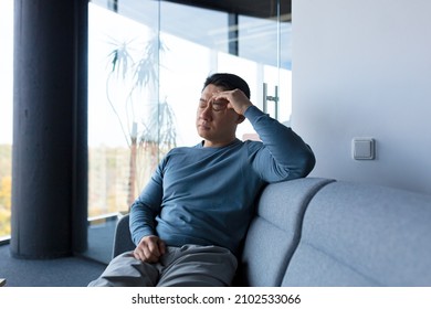 Tired and pensive Asian worker, resting on the office sofa, in a modern office, a businessman makes a difficult and fateful decision - Powered by Shutterstock