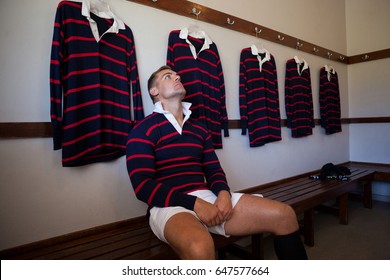 Tired player wearing jersey sitting on bench against wall in locker room - Powered by Shutterstock