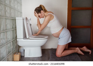 Tired Pregnant Woman With Headache Holing Head Using Palm Vomit To The Toilet Standing On Her Knees In The Bathroom