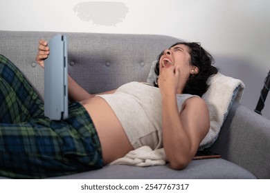 Tired pregnant woman yawning while using digital tablet on sofa at night, suffering from insomnia - Powered by Shutterstock