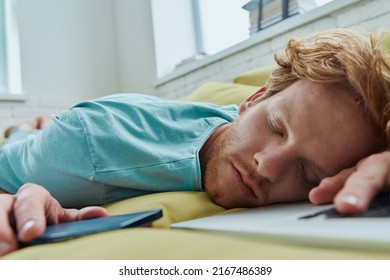 Tired Redhead Man Napping On The Couch With Laptop And Smart Phone Laying Near Him