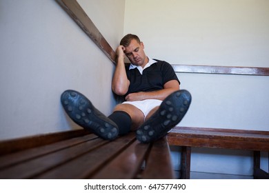 Tired rugby player leaning on wall while sitting on bench at locker room - Powered by Shutterstock