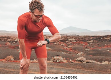 Tired Runner Man Checking Wearable Technology Sports Smartwatch During Outdoor Training. Sport Athlete Looking At Watch During Workout On Desert Trail. Man Wearing Sunglasses, Compression Outfit.