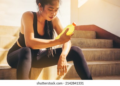 Tired runner woman with a bottle of electrolyte drink freshness after training outdoor workout at the stadium stairway. - Shutterstock ID 2142841331