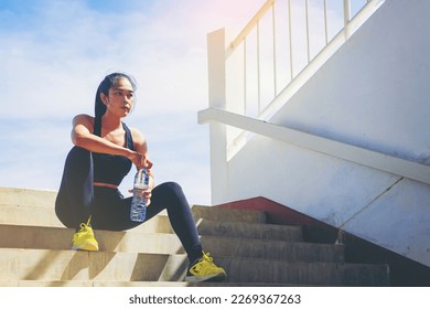 Tired runner woman with a bottle of electrolyte drink freshness after training outdoor workout at the stadium stairway. - Powered by Shutterstock