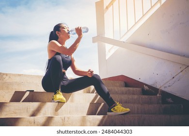 Tired runner woman with a bottle of electrolyte drink freshness after training outdoor workout at the stadium stairway. - Powered by Shutterstock