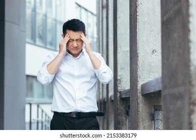 Tired and sad Asian has a severe headache, a businessman outside the office, holding hands behind his head