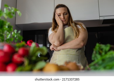 Tired, Sad And Bored Plus Size Blond Woman Holding Head In Hand, Thinking What To Cook, Have No Idea. Diet And Healthy Eating With Vegetables. Home Cooking, Looking For Recipe. Greenery On Foreground