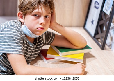 A Tired Sad Boy Lies On A Stack Of Books, Studying At Home At His Desk. Home Education. Coronavirus Epidemic Covid-19. The Child Is Doing Homework. Homeschooling. Quarantine. Overwork And Health