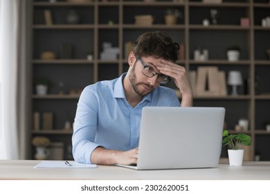 Tired sad freelancer man getting problems with laptop, software error, feeling stress, exhaustion, headache, touching head at home work table, looking at screen with doubt - Powered by Shutterstock