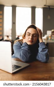 Tired Sad Woman With Glasses Working In The Cafe. Feeling Mental Illness And Stress After Overwork. Freelance Girl Working In A Cafe. The Girl Works Remotely. Work Remotely. Online Learning. Remote.