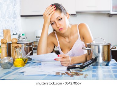 Müde und traurige junge Frau, die Rechnungen in der Küche liest