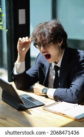 Tired salaryman works on his digital tablet computer and feels sleepy at his workstation. overworked - Shutterstock ID 2068471436