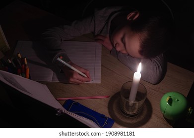 Tired schoolboy with candle in complete darkness doing homework. Power outage, blackout, concept image. 