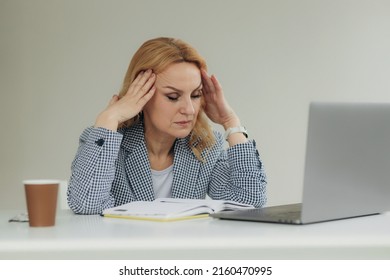 Tired senior business woman is using laptop for work indoor. A beautiful older lady has headache from overworking. Mature woman 50s. Close-up portrait businesswoman